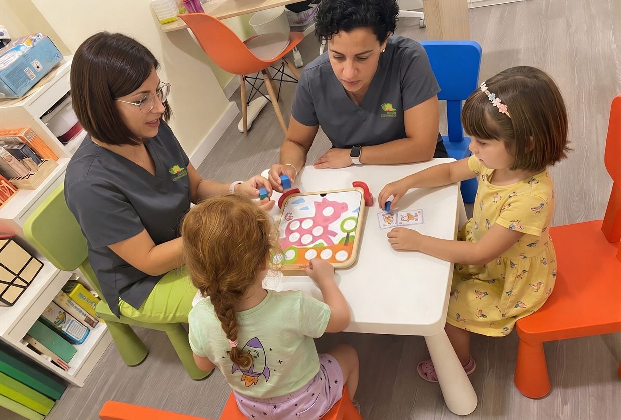 Dos terapeutas de anda CONMiGO trabajando en mesa con dos niñas